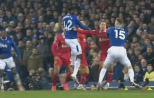 Zawodnicy Evertonu i Liverpoolu walczą o piłkę podczas zaciętego meczu derbowego. Intensywna rywalizacja na boisku, w tle kibice na trybunach. Everton vs Liverpool skrót meczu