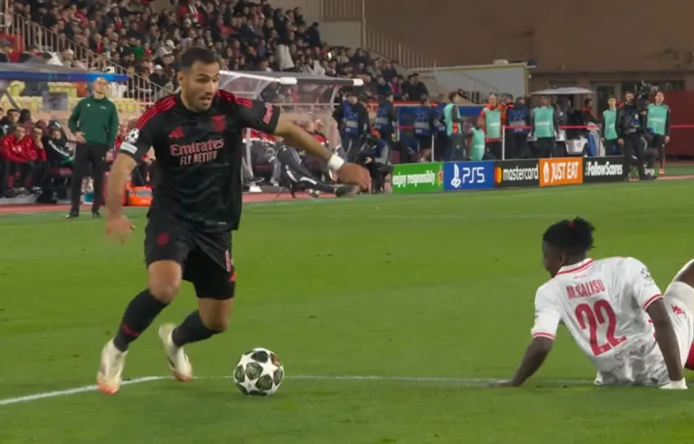 Piłkarze AS Monaco i Benfiki rywalizują o piłkę podczas meczu Ligi Mistrzów. Dynamiczna akcja na boisku, zawodnicy w pełnym skupieniu.