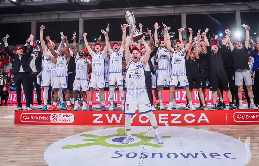 Zawodnicy Górnika Zamek Książ Wałbrzych w trakcie finałowego meczu Pekao S.A. Pucharu Polski. Dynamiczna akcja na parkiecie, koszykarze w pełnym skupieniu walczą o zwycięstwo. W tle kibice i hala sportowa.