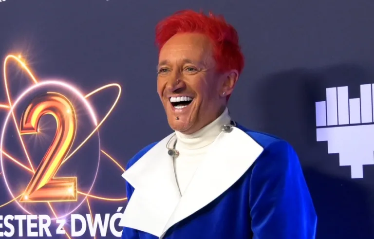 Artysta z charakterystycznymi czerwonymi włosami uśmiecha się na ściance podczas Sylwestra z Dwójką TVP