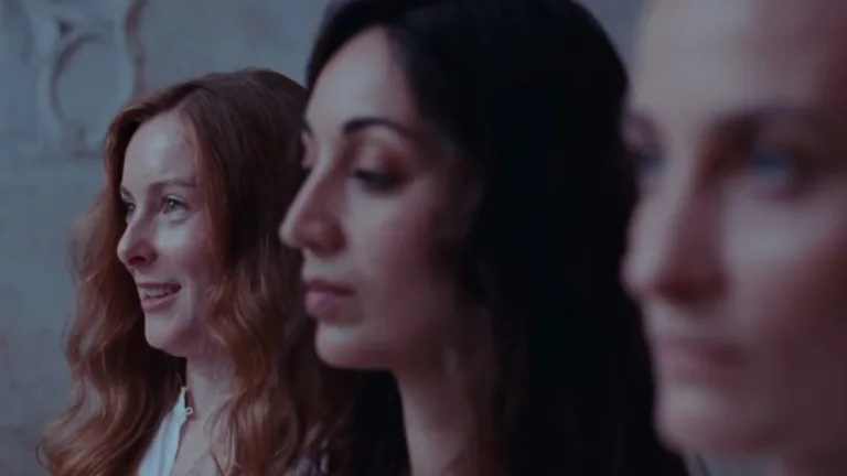 Trzy bohaterki filmu Glorious Summer siedzą obok siebie w półcieniu pałacowego wnętrza, patrząc przed siebie z pozornym spokojem