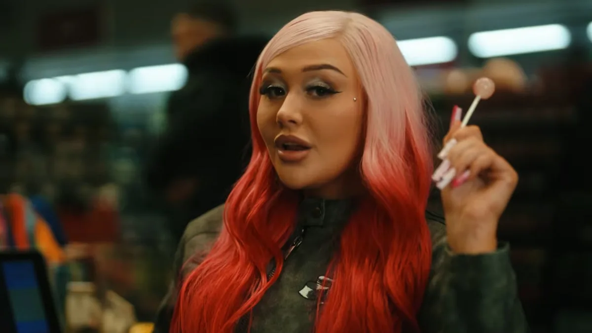 Artystka Oliwka Brazil z różowo-czerwonymi włosami trzyma lizaka, stojąc we wnętrzu sklepu.