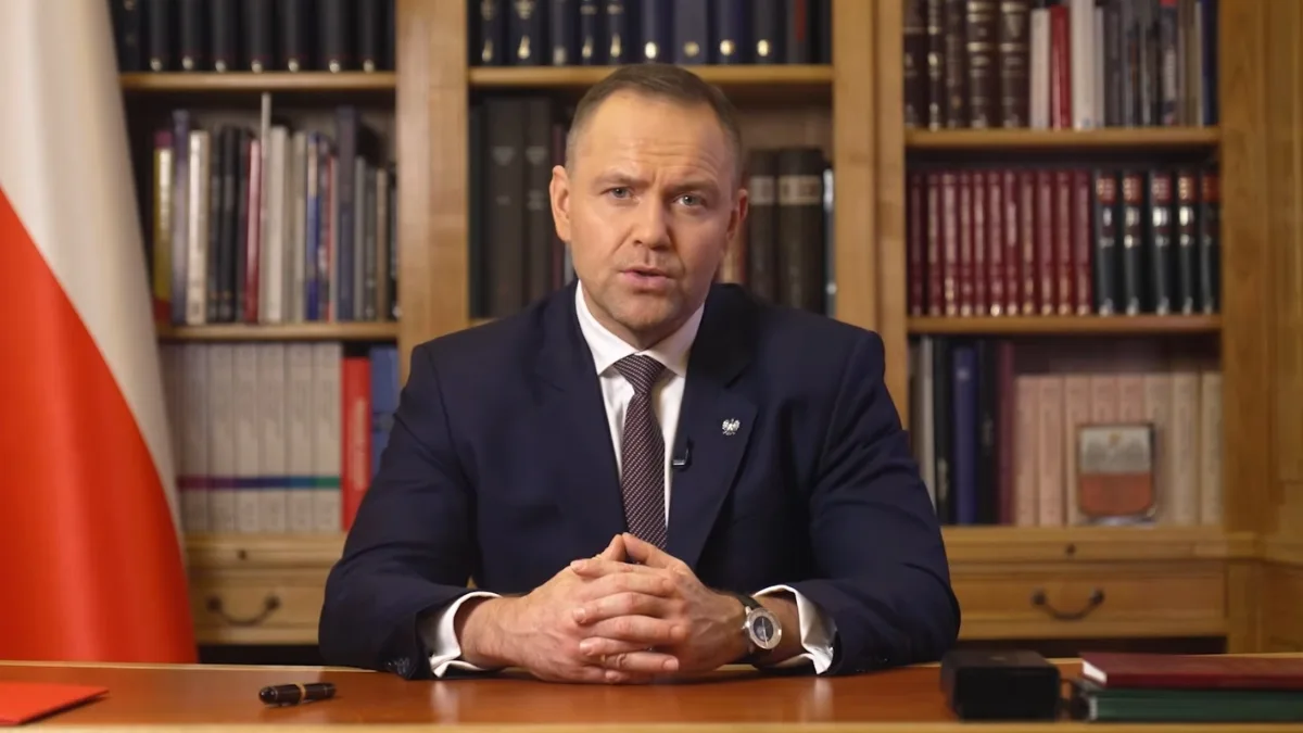 Karol Nawrocki wygłasza oficjalne wystąpienie w gabinecie, siedząc przy biurku na tle biblioteczki i flagi Polski.