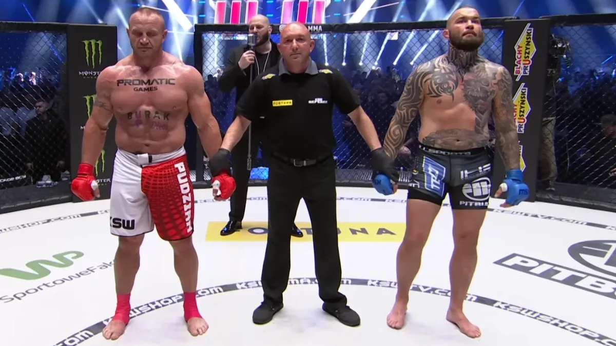 Pudzianowski i Materla stoją naprzeciw siebie w klatce, trzymanych za ręce przez sędziego przed ogłoszeniem werdyktu podczas gali sportów walki.