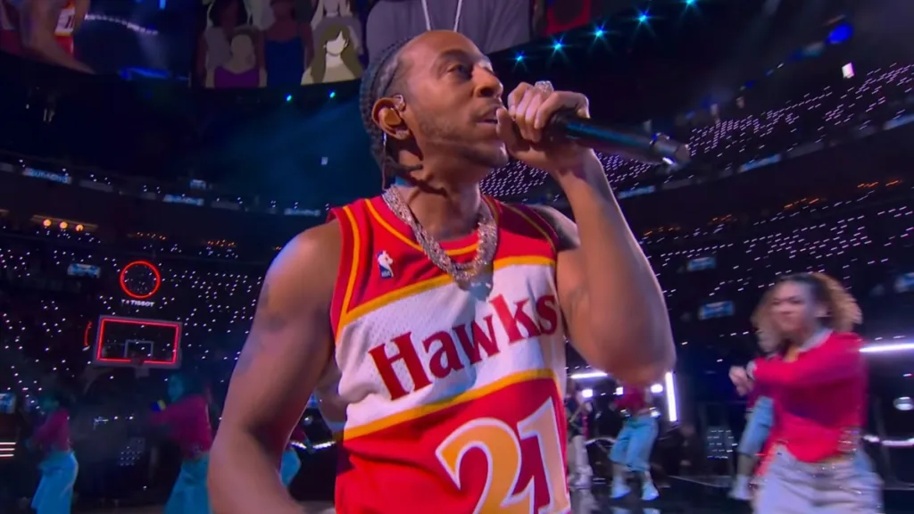 Ludacris występuje na parkiecie NBA w koszulce Atlanta Hawks nr 21, trzymając mikrofon podczas All-Star Saturday Night.