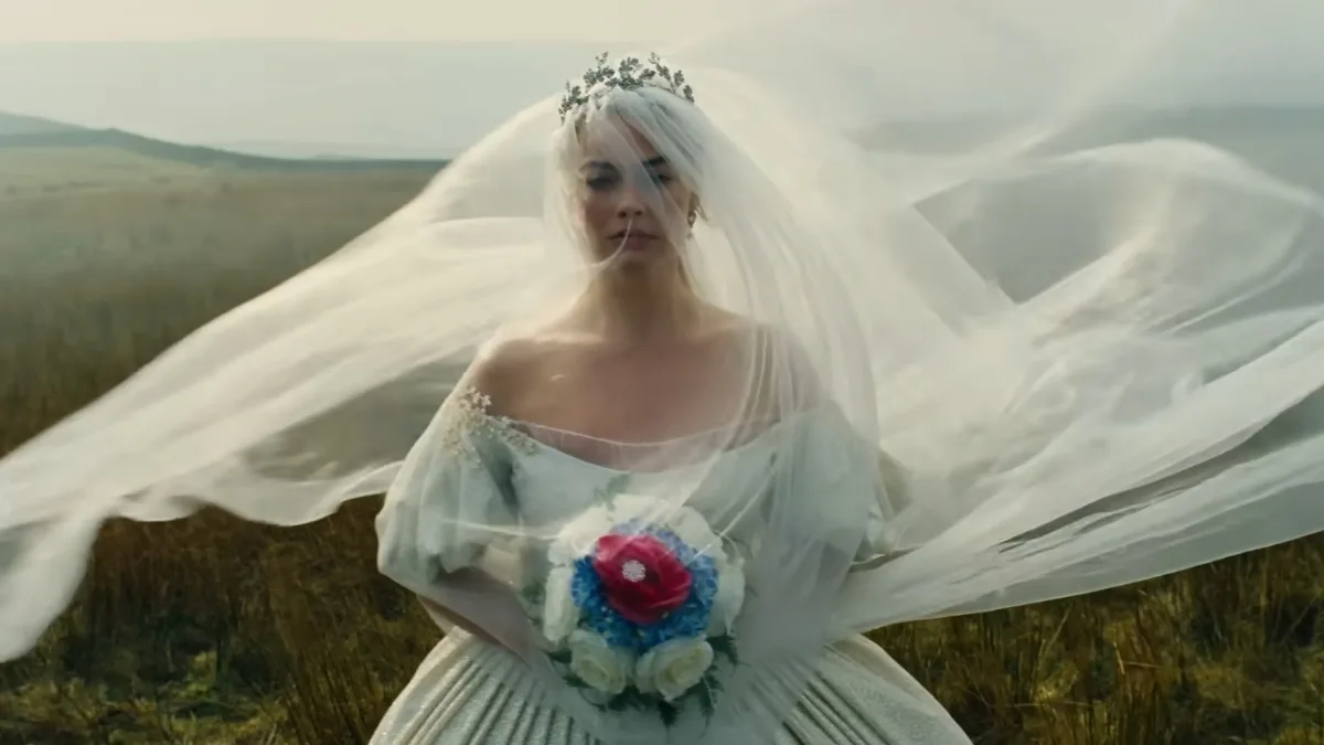Margot Robbie w białej sukni ślubnej z rozwianym welonem stoi na wrzosowiskach - kadr z filmu Wichrowe wzgórza (2026).