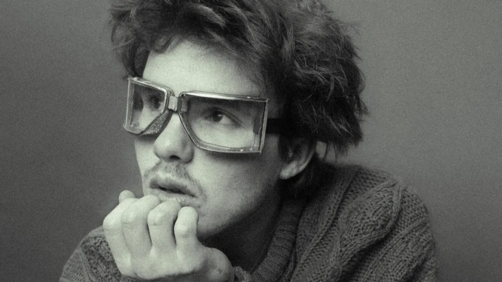 Cruz Beckham - For Your Love: czarno-białe zbliżenie artysty w dużych, kwadratowych okularach, patrzącego w bok w refleksyjnej pozie.