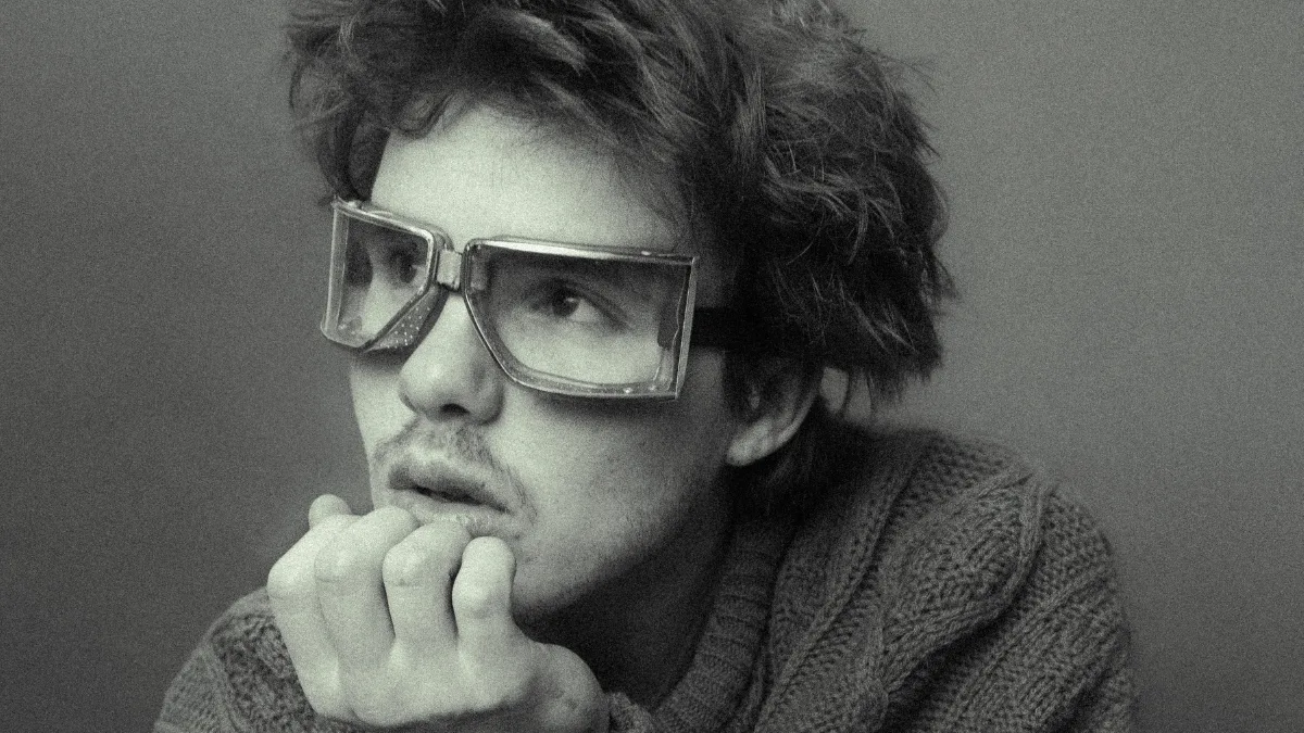 Cruz Beckham - For Your Love: czarno-białe zbliżenie artysty w dużych, kwadratowych okularach, patrzącego w bok w refleksyjnej pozie.