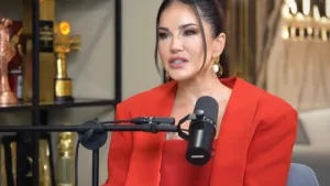 Sunny Leone w czerwonym garniturze podczas wywiadu, siedzi przed mikrofonem w studiu nagraniowym.