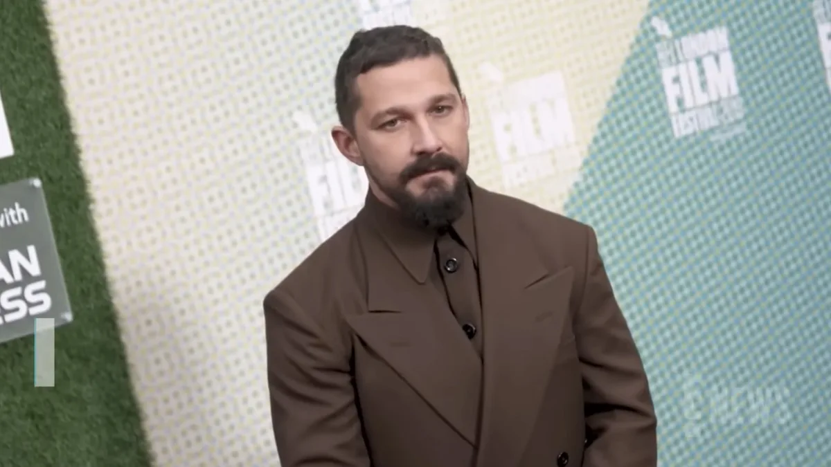 Shia LaBeouf na czerwonym dywanie w brązowym garniturze podczas wydarzenia filmowego.
