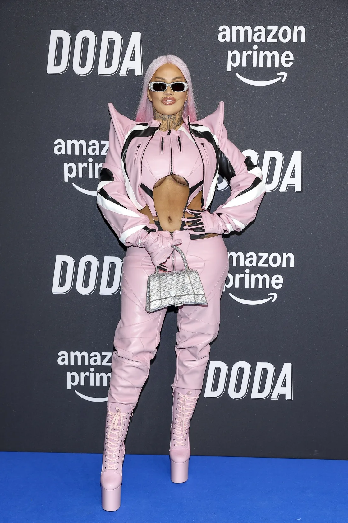 Laluna w różowym, futurystycznym komplecie z wycięciami i wysokimi platformami pozuje na tle ścianki z logo Amazon Prime i napisem Doda podczas premiery serialu.