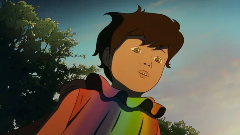 Chłopiec z Arco w kolorowej pelerynie patrzy w dół z zaskoczeniem, w tle drzewa i ciepłe światło zachodzącego słońca.