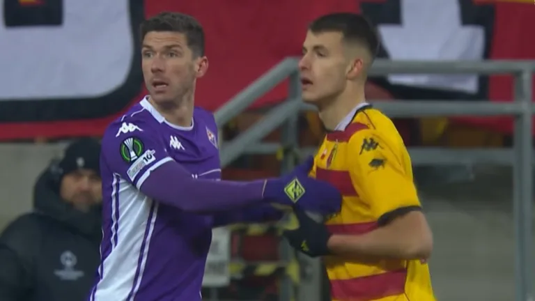 Zawodnik Fiorentiny w fioletowej koszulce trzyma rywala z Jagiellonii Białystok w żółto-czerwonym stroju podczas walki o pozycję w polu karnym.