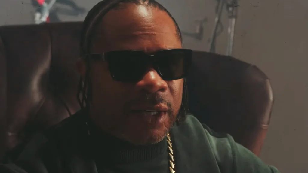 Xzibit w ciemnych okularach siedzi w fotelu w kadrze z teledysku History