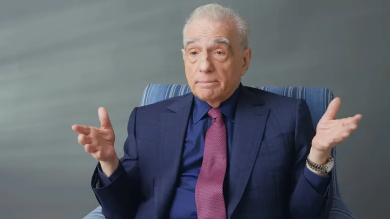 Martin Scorsese siedzi w fotelu podczas wywiadu, ubrany w granatowy garnitur i czerwony krawat, gestykulując rękami.