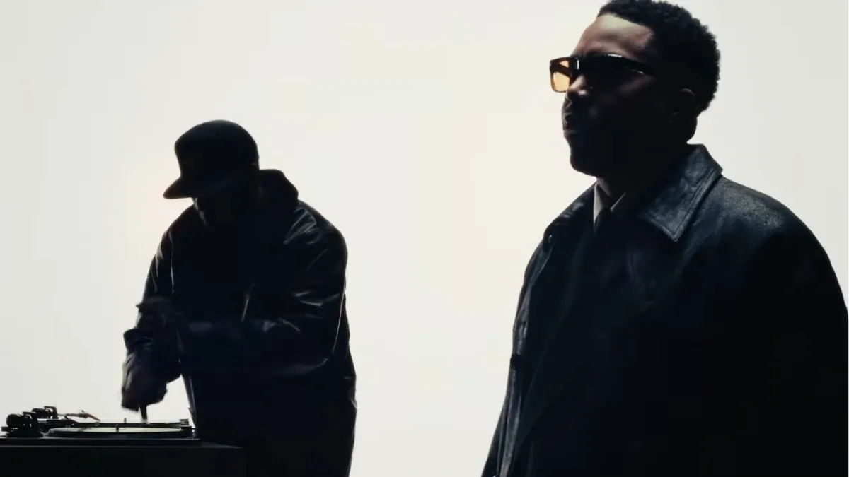 Nas i DJ Premier w minimalistycznym ujęciu z teledysku GiT Ready, Premier przy gramofonach, Nas w eleganckiej stylizacji na jasnym tle.