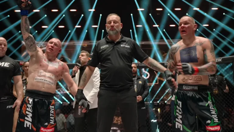 Michał „Matrix” Królik z uniesioną ręką ogłoszony zwycięzcą walki, obok niego stoi sędzia oraz pokonany Michał Pasternak w klatce podczas gali FAME 30 w Gliwicach.
